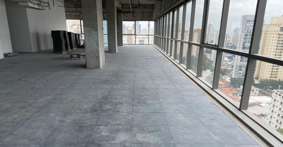 Amplo salão comercial em obras com placas instaladas de piso elevado e piso suspenso.