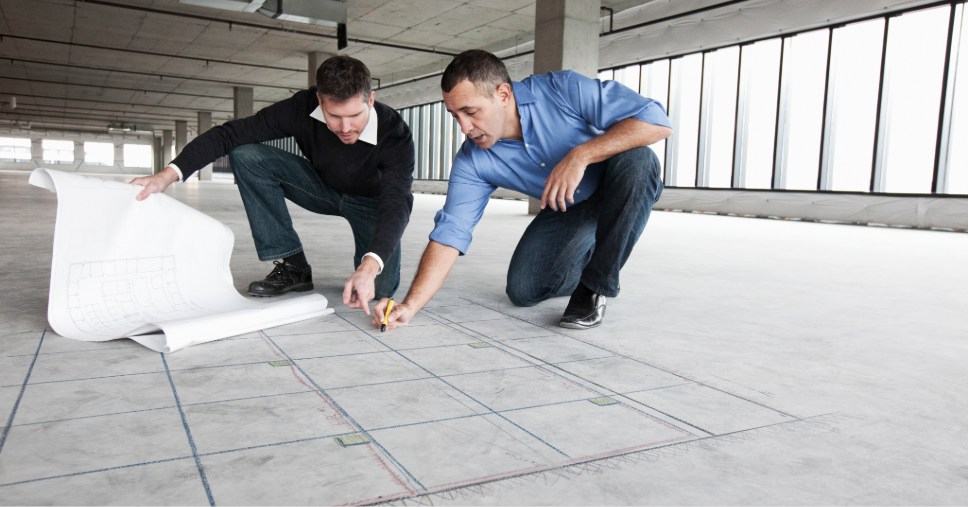 Engenheiros analisando a planta em um canteiro de obras para o planejamento para piso elevado.